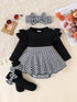 Black and white baby outfit with ruffled long-sleeve top, houndstooth skirt, socks, and headband on a textured surface.