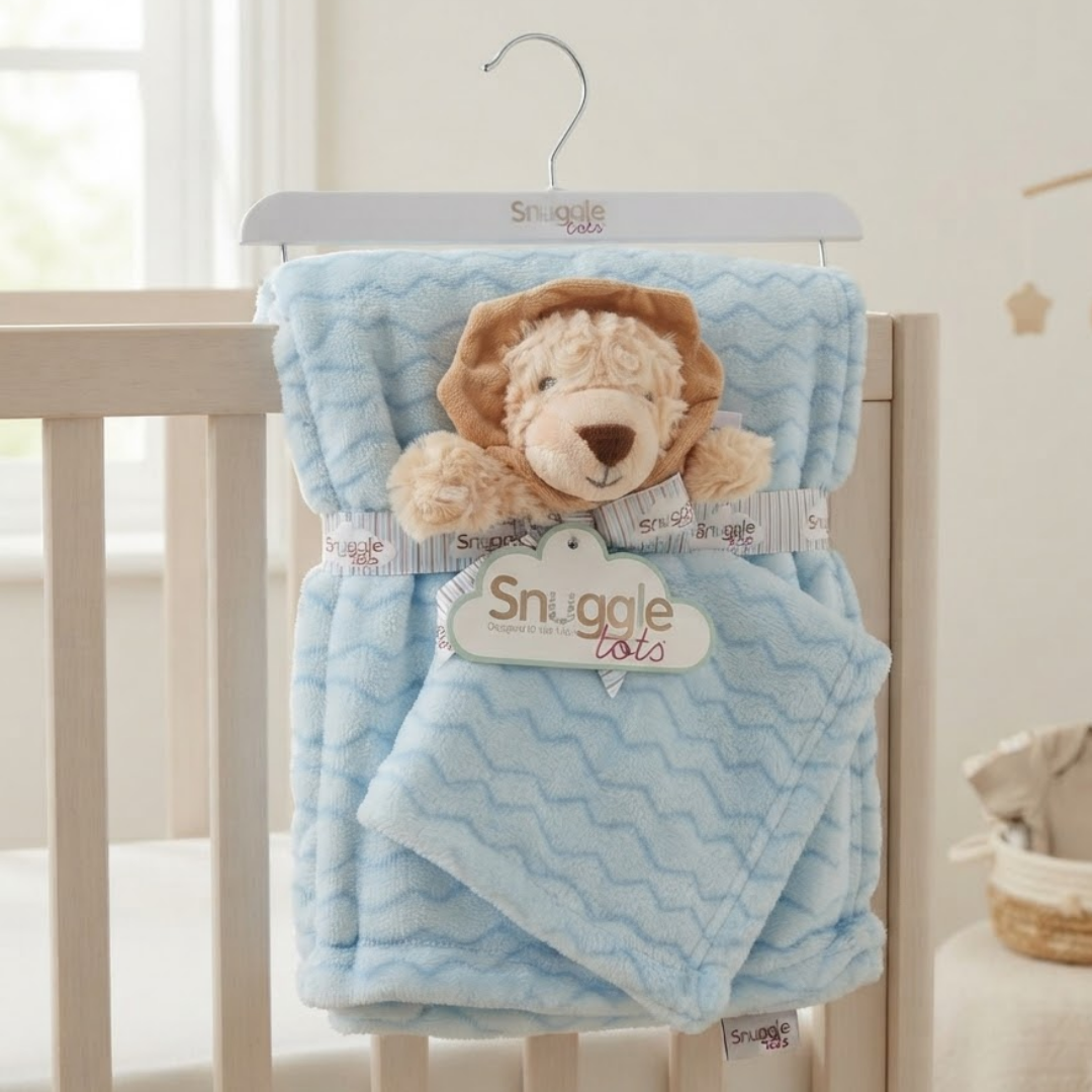 A Snuggle LOTS baby blanket set in a light blue chevron pattern, featuring a plush lion toy and a hanging tag, displayed on a white hanger draped over a white wooden baby crib.