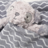 A soft, fluffy light gray stuffed animal toy peeking out from a gray blanket with a white chevron pattern.