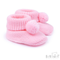 A pair of light pink knit baby booties with matching pom-poms, shown on a clean white background with a Soft Touch Babywear logo in the bottom right corner.