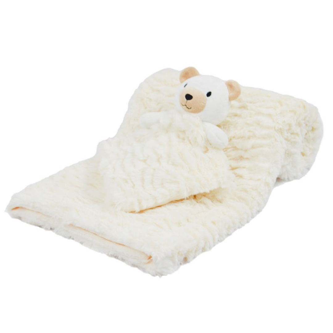 A soft cream-colored textured blanket with a small plush teddy bear attached at one end, photographed on a plain white background.
