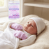 Newborn baby wrapped in white blanket with pink mittens, wearing a white hat, with a package of soft touch mittens in the background.