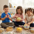 Three children playing with wooden toys on a rug in a room with books and toys in the background.