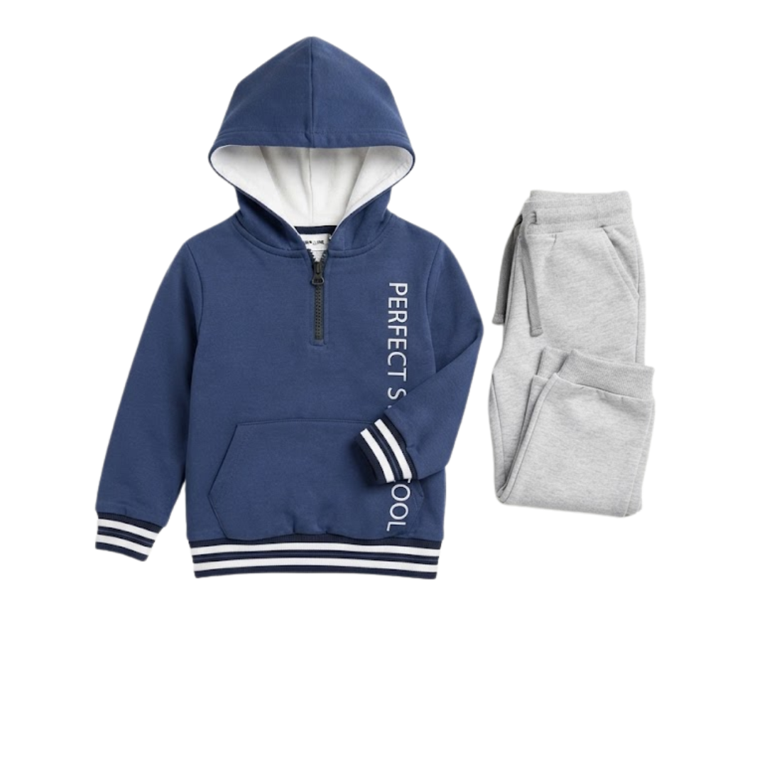 A baby two-piece knit outfit set laid flat on a cream satin fabric background. The set includes a long-sleeve top with a white body, light blue yoke and cuffs, and a blue train graphic on the chest, paired with matching light blue pants with white cuffs.