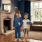 Two children standing in a room with a fireplace and large window.