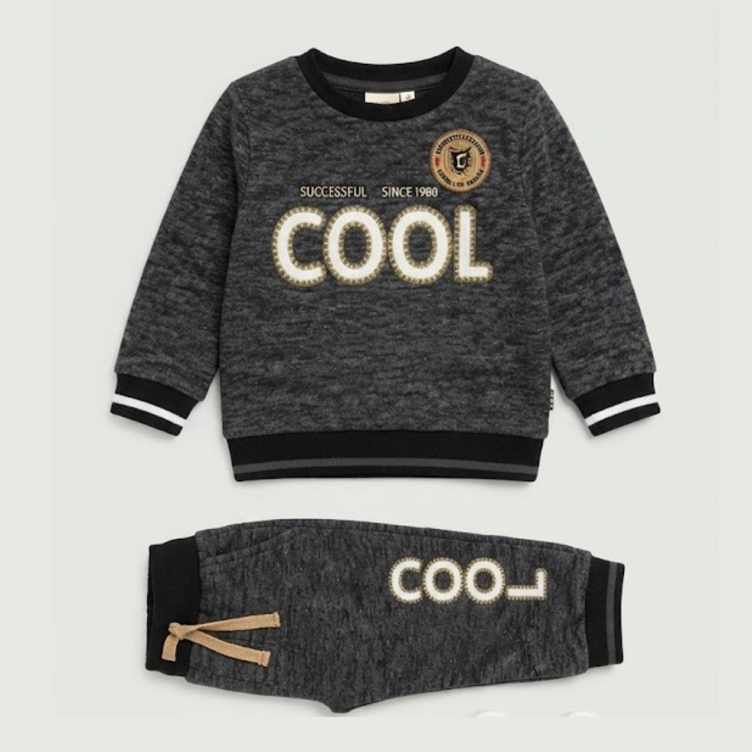 A two-piece kids' lounge set consisting of a long-sleeve sweatshirt and matching jogger pants in dark heather gray. The sweatshirt features 'COOL' printed across the chest in a cream-colored textured font, with a circular crest logo on the upper right chest.