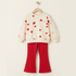 A children's two-piece outfit hanging on a wooden hanger against a plain light beige wall. The set includes a cream sweatshirt with red heart prints and the word 'love' on the chest, paired with bright red flared pants.