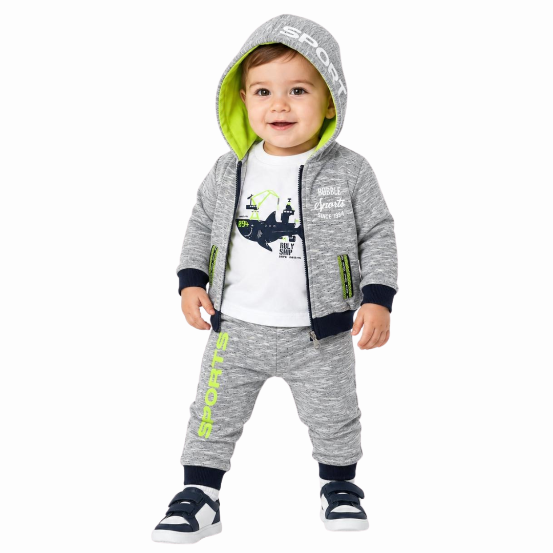 A toddler wearing a heather gray two-piece tracksuit with a zip-up hoodie and matching joggers, featuring a white graphic t-shirt underneath and navy sneakers, photographed against a solid white background.