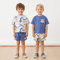 Two young boys wearing matching outfits with blue and white patterns on a plain background