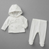 A baby clothing set consisting of a white hooded wrap jacket with a subtle gray pattern and matching white footed leggings with bear face toe caps, laid flat on a neutral gray background.
