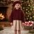 A young girl stands in front of a decorated Christmas tree and fireplace wearing a burgundy sherpa cropped jacket, a matching burgundy beret, and a beige and white gingham skirt.