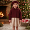 A young girl stands in front of a decorated Christmas tree and fireplace wearing a burgundy sherpa cropped jacket, a matching burgundy beret, and a beige and white gingham skirt.
