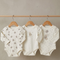 Three baby bodysuits with bear patterns on wooden hangers against a neutral background