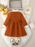 Brown corduroy dress with white trim on a textured surface with decorative items.