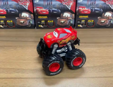 Toy car with large wheels on a wooden surface, with packaging in the background.