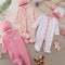 Collection of baby clothing and accessories on a neutral background with flowers.