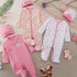 Collection of baby clothing and accessories on a neutral background with flowers.