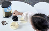 Person using a portable coffee maker on a white surface with coffee beans nearby.