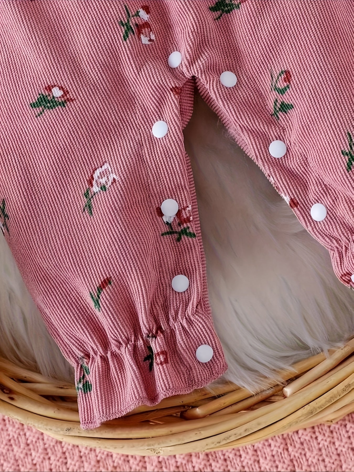 Pink baby romper with floral patterns on a woven basket