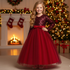 Young girl in a red dress standing in front of a Christmas tree and fireplace.