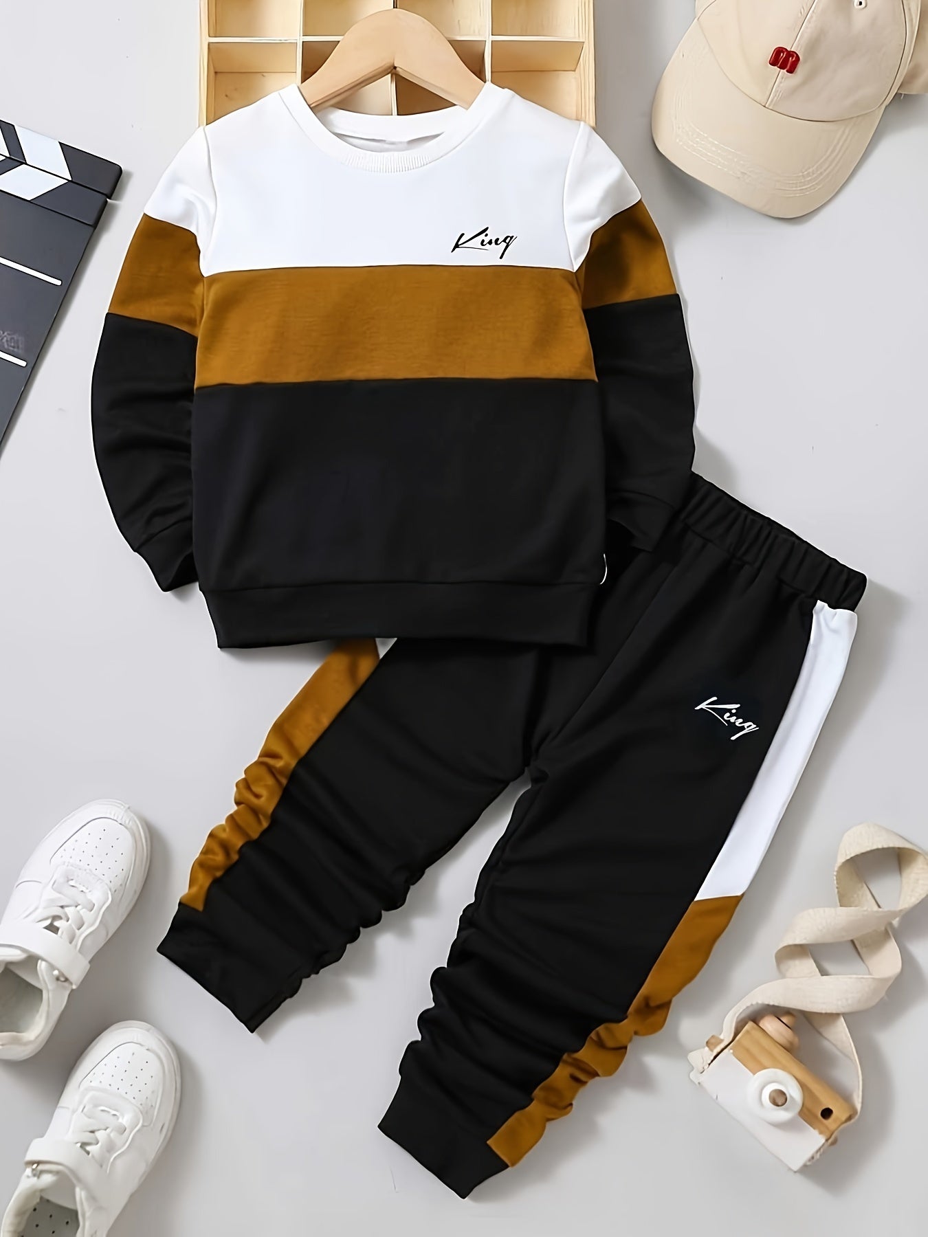 Children's black and brown striped sweatshirt and pants set with white sneakers on a light gray background.