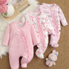 Three pink baby onesies with bow patterns on a textured surface.
