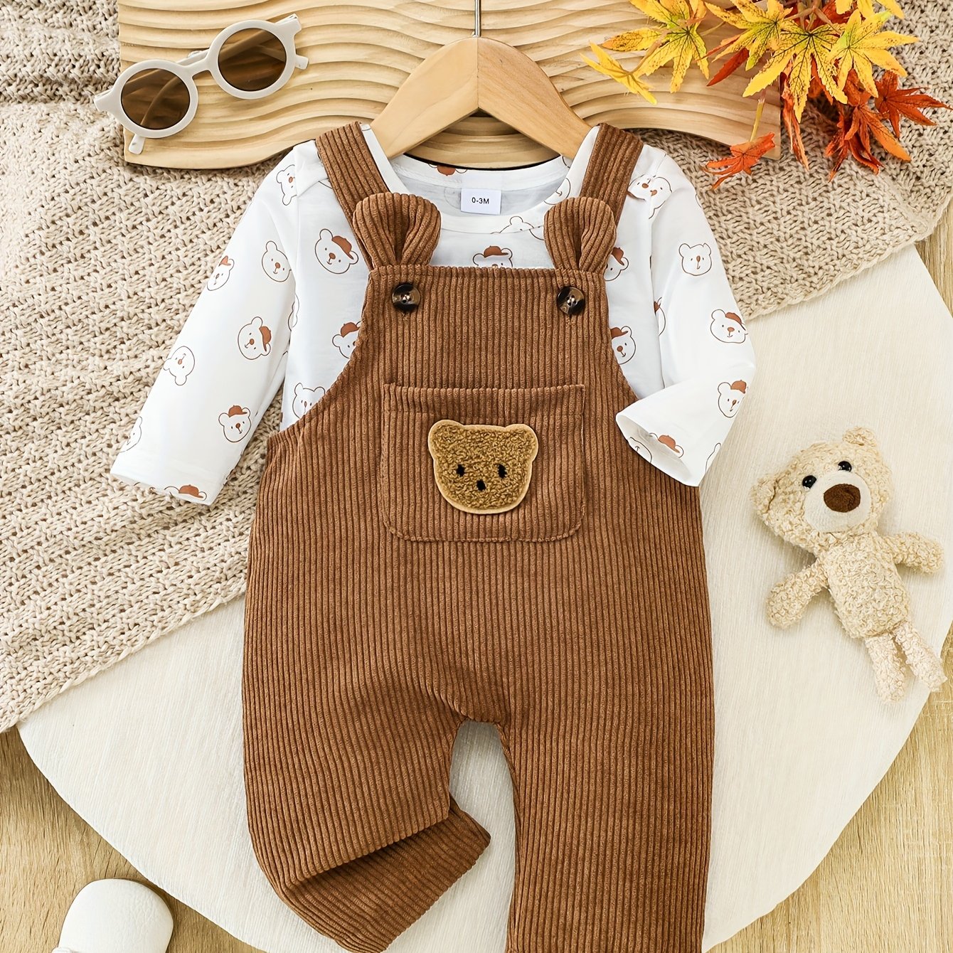 Baby outfit with brown overalls and white shirt with bear pattern on a wooden surface.