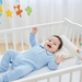 Baby in a blue outfit lying in a crib with colorful hanging toys in the background