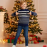 Child in a striped sweater standing in front of a decorated Christmas tree with presents.
