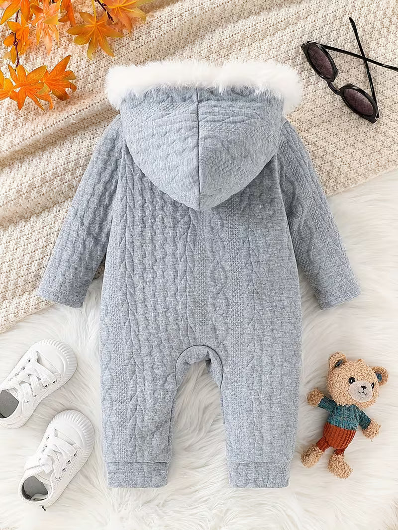 Gray baby romper with fur hood on a textured surface with shoes and a teddy bear.