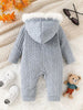 Gray baby romper with fur hood on a textured surface with shoes and a teddy bear.