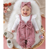 Baby in pink romper with floral patterns and matching headband on a soft surface with flowers.