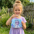 Young girl holding a Frozen-themed purse and necklace in a garden setting